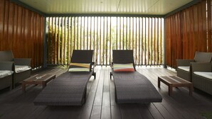 Un área lounge exterior moderna con mobiliario de mimbre, suelo de madera y persianas verticales.