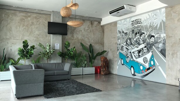 Un salon moderne avec un canapé gris, un tapis noir et une grande fresque murale représentant une voiture bleue avec des personnes à l’intérieur.