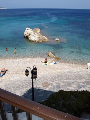 A beach with clear blue water, rocky formations, and a few people sunbathing. - Lemos Hotel (Samos)