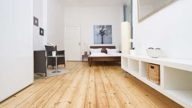 A modern bedroom with a wooden floor, a bed with white bedding, a bedside table, a chair, a small table, and a wall-mounted mirror. - Primeflats - Apartment in Pankow (Berlin)