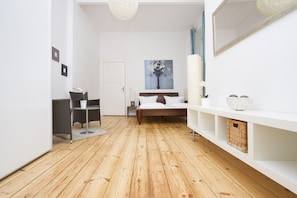 Ein modernes Schlafzimmer mit Holzboden, einem Bett mit weißer Bettwäsche, einem Nachttisch, einem Sessel, einem kleinen Tisch und einem wandmontierten Spiegel.