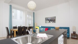 A modern kitchen with a large island, a built-in washing machine, and a dining area with a wooden table and chairs. - Primeflats - Apartment in Pankow (Berlin)