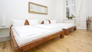 A double bed with white linens, a wooden headboard, a bedside table, a mirror, a window with sheer curtains, and a small plant on the windowsill. - Primeflats - Apartment in Pankow (Berlin)