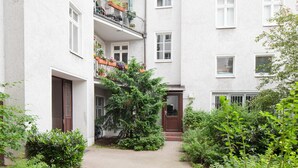 A multi-story residential building with balconies, a small garden area, and a door with a brown frame. - Primeflats - Apartment in Pankow (Berlin)