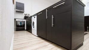 A modern kitchen with dark cabinetry, a built-in oven, a washing machine, and a stainless steel range hood. - Primeflats - Apartment in Pankow (Berlin)