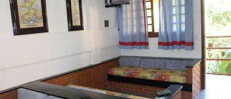 A room with a brick wall, a bench, a television mounted on the wall, and a window with curtains.
