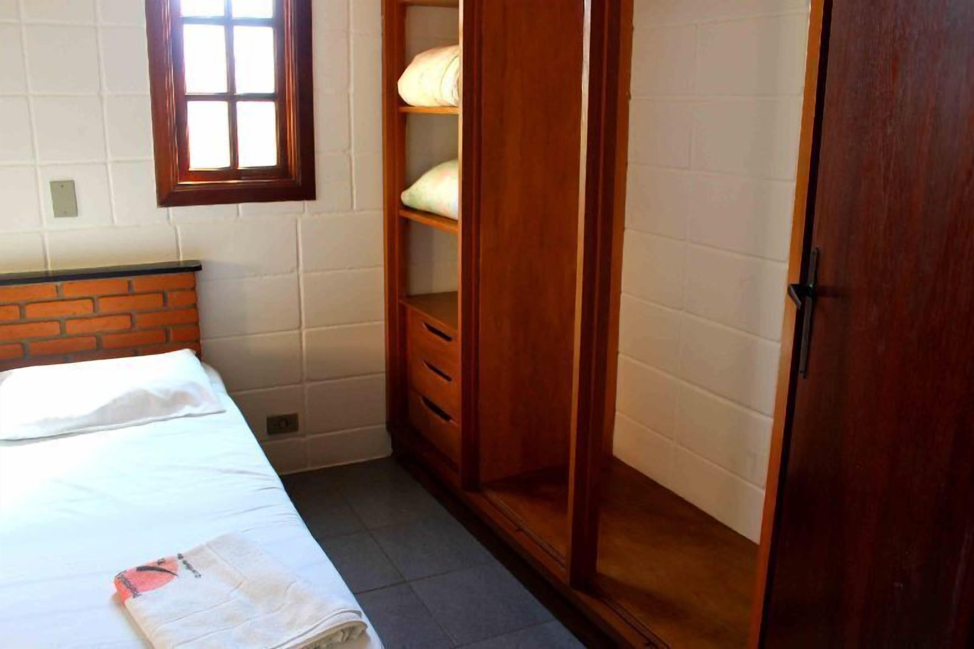 Una habitación pequeña y bien iluminada con una cama individual, un armario de madera y una ventana.