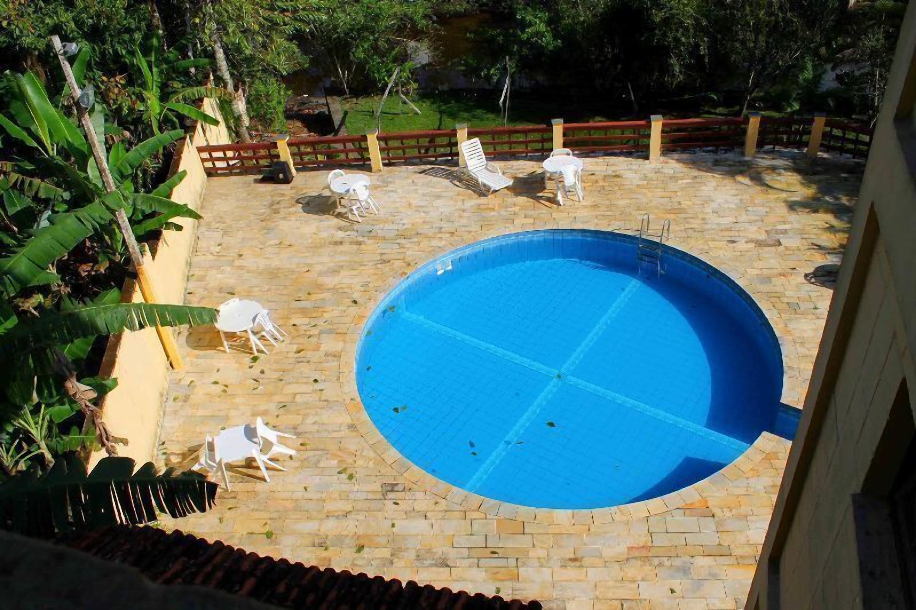 A circular pool with a tiled deck, surrounded by white lounge chairs and a wooden fence.