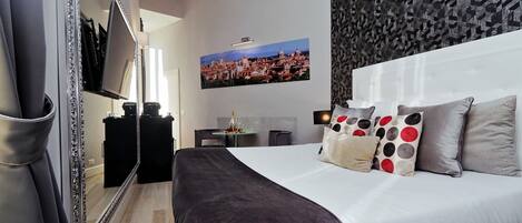 A hotel room with a large bed, a TV, a desk, and a cityscape painting on the wall.