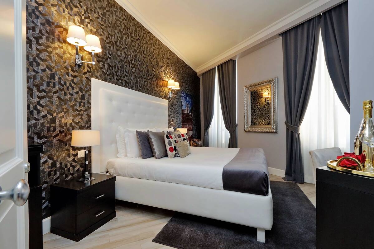 A modern bedroom with a large bed, a nightstand, a dresser, and a wall-mounted lamp.