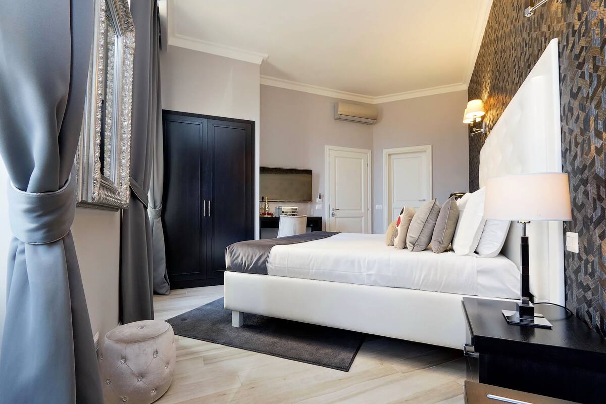 A modern bedroom with a large bed, a wardrobe, a desk, and a bathroom.