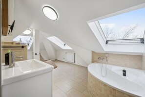 A modern bathroom with a skylight, a bathtub, and a large sink. - Limehome Dresden Antonstraße (Dresden)