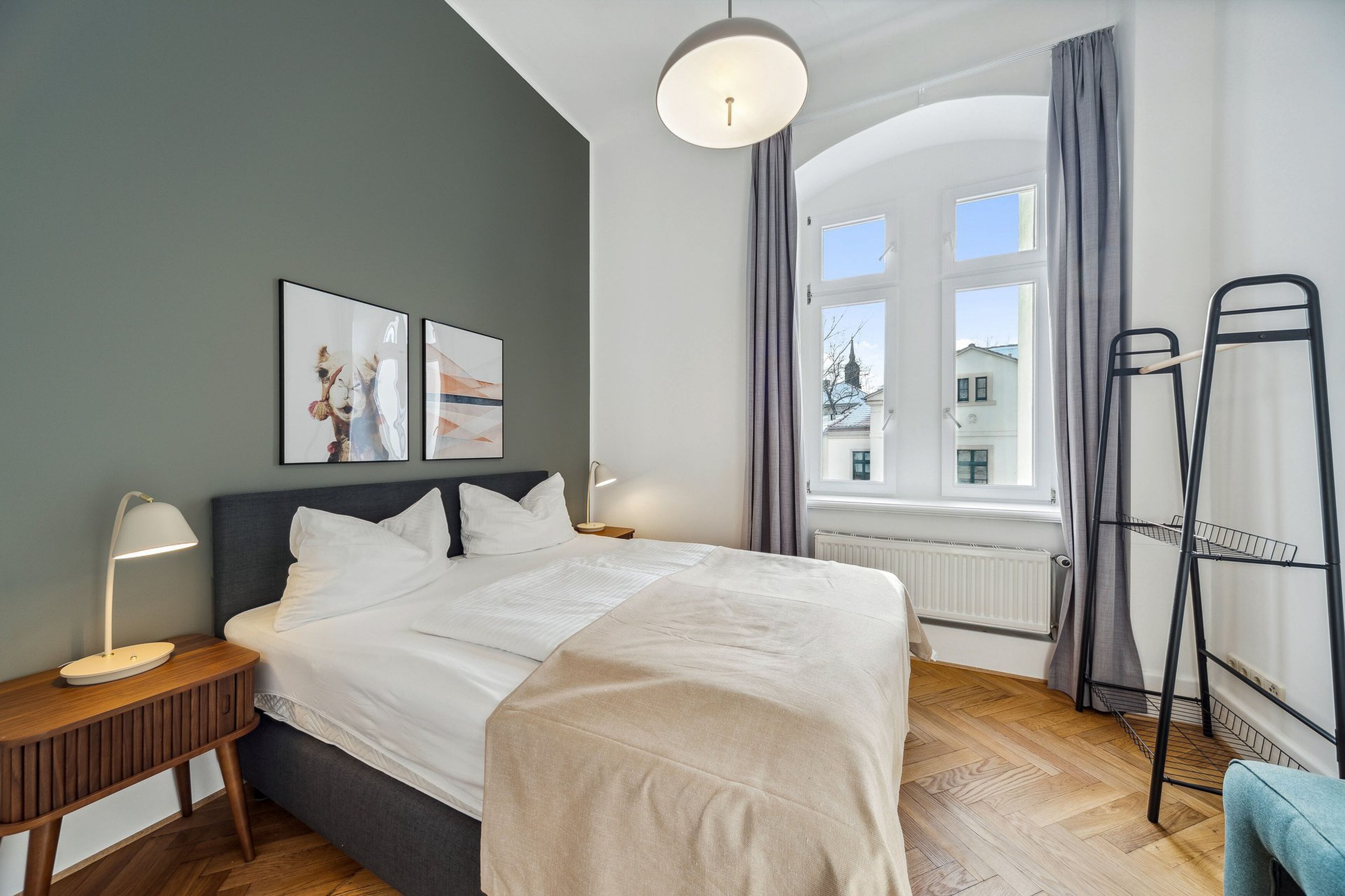 A neatly arranged bedroom with a bed, bedside tables, a window with curtains, and a radiator.