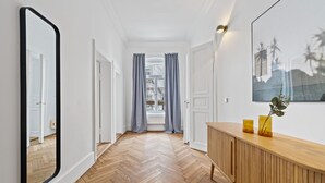 Un couloir doté d’un parquet en bois disposé en motif «chevrons», de murs blancs, d’une console en bois ornée de vases jaunes et d’un grand miroir sur le côté gauche.