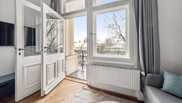 Une pièce avec une grande porte ouverte donnant sur un balcon, un canapé gris et un radiateur.