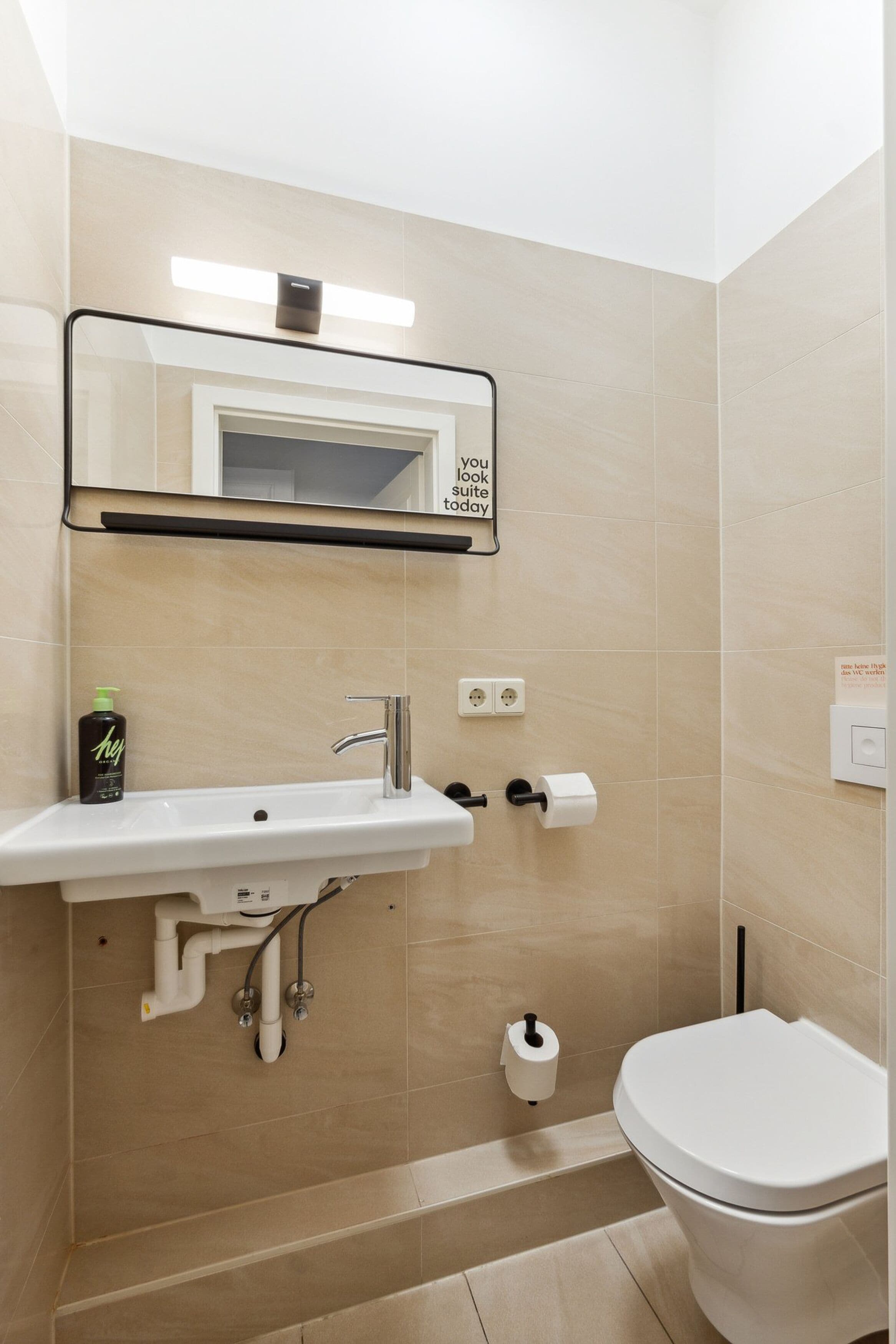 Un bagno con lavandino, specchio, WC ed erogatore di asciugamani.