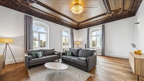 Un salon spacieux avec deux canapés gris, une table basse blanche et un parquet en bois à motifs chevrons.