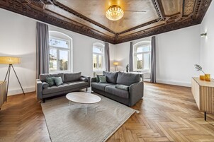 A spacious living room with two grey sofas, a white coffee table, and a herringbone wooden floor.