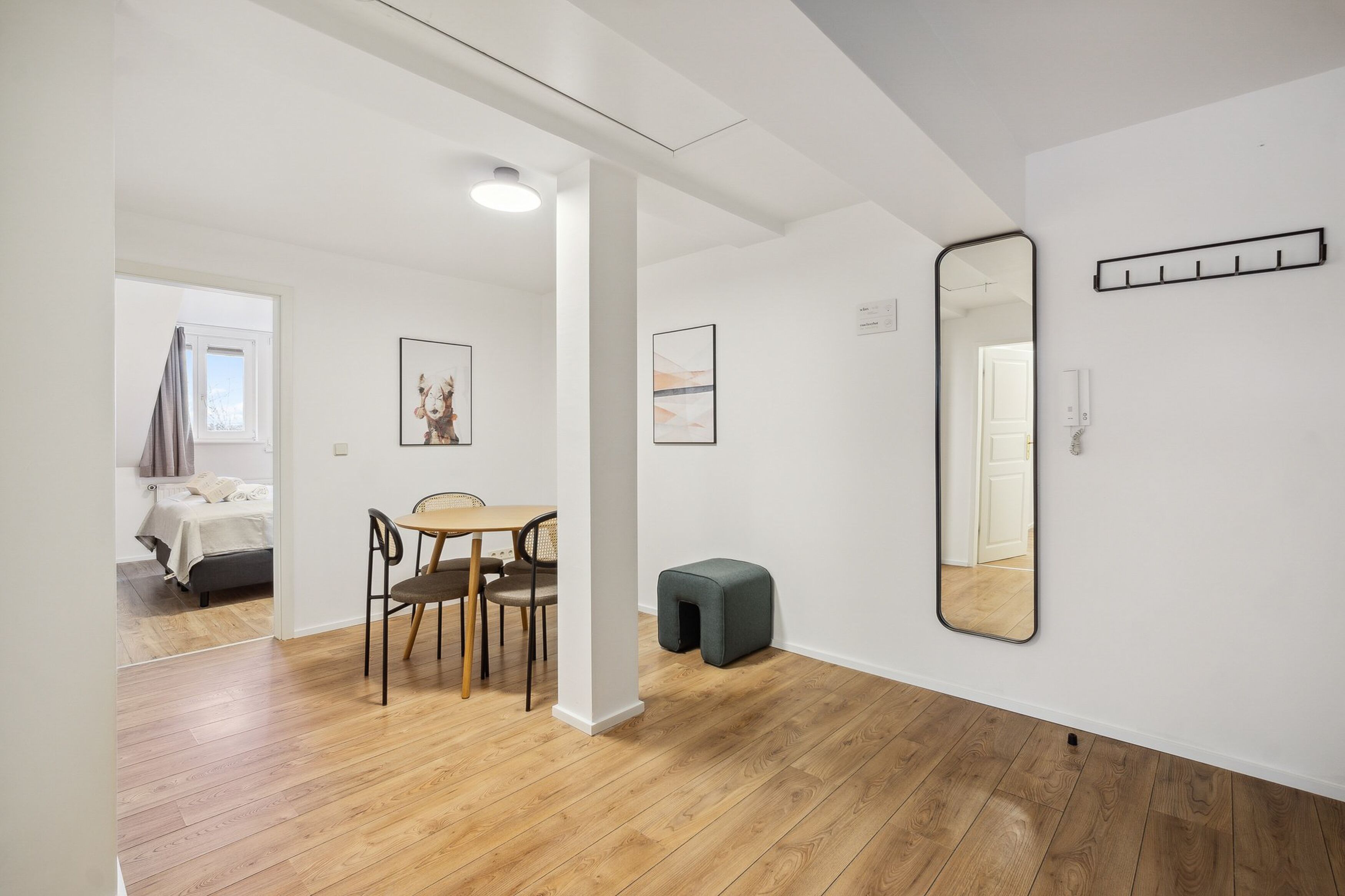 A modern, well-lit room with wooden flooring, a dining area with a table and chairs, a large mirror, and artwork on the walls.