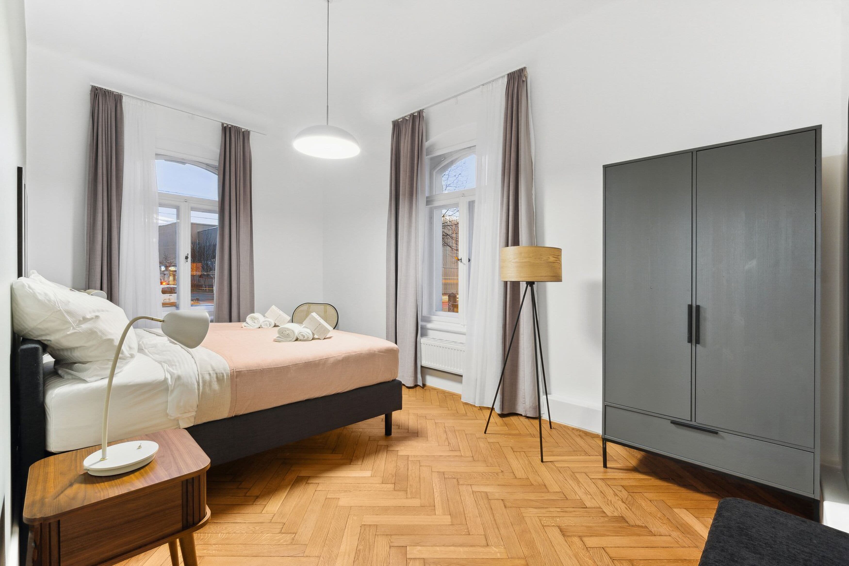 A modern bedroom with a bed, bedside table, lamp, wardrobe, and large windows.