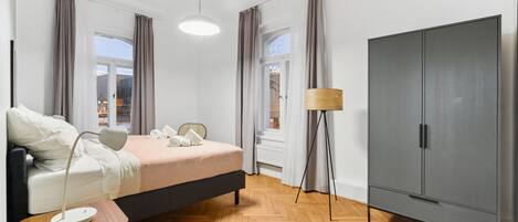A modern bedroom with a bed, bedside table, lamp, wardrobe, and large windows.
