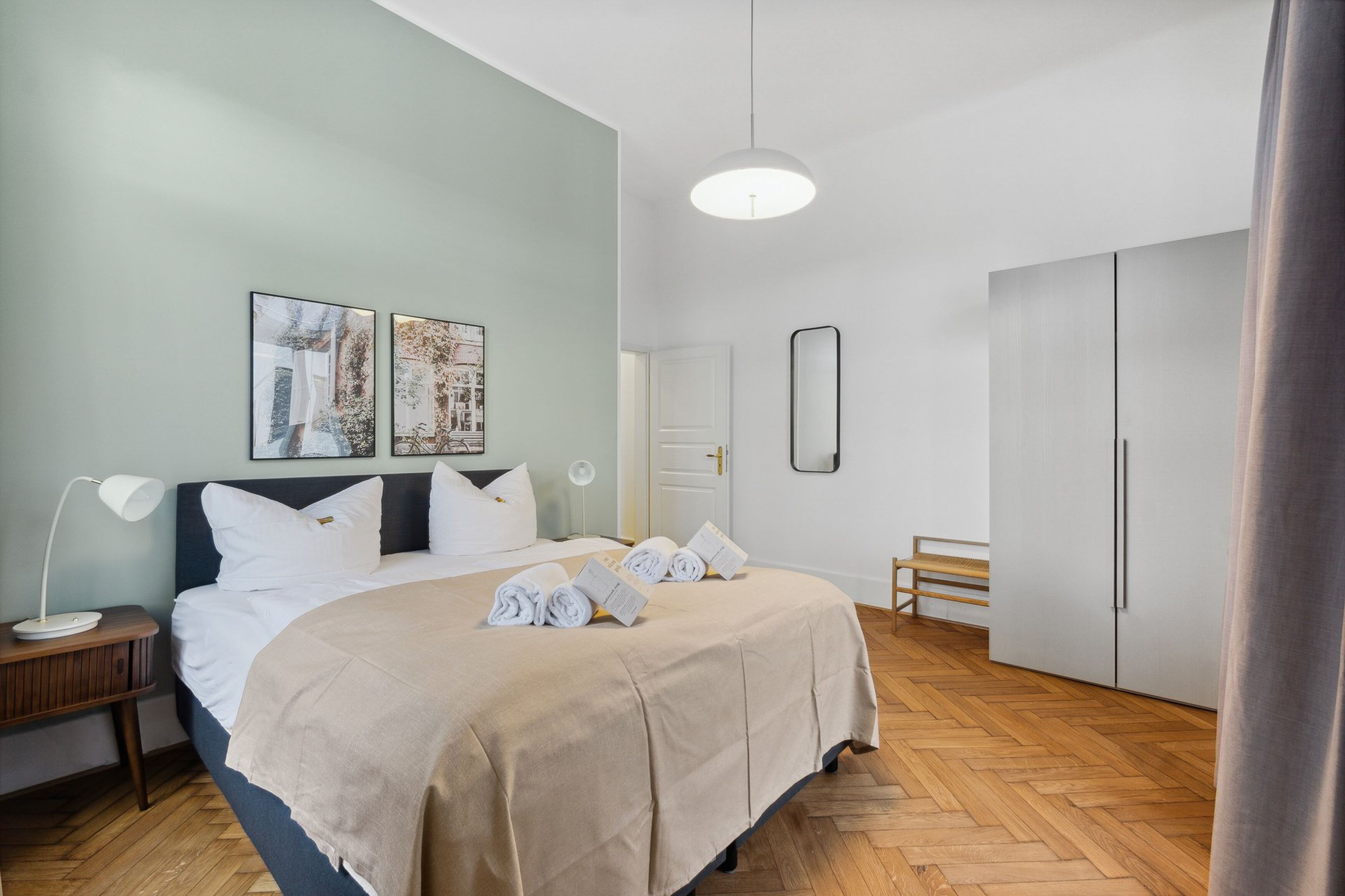 A neatly arranged hotel room with a bed, bedside table, lamp, and artwork on the wall.