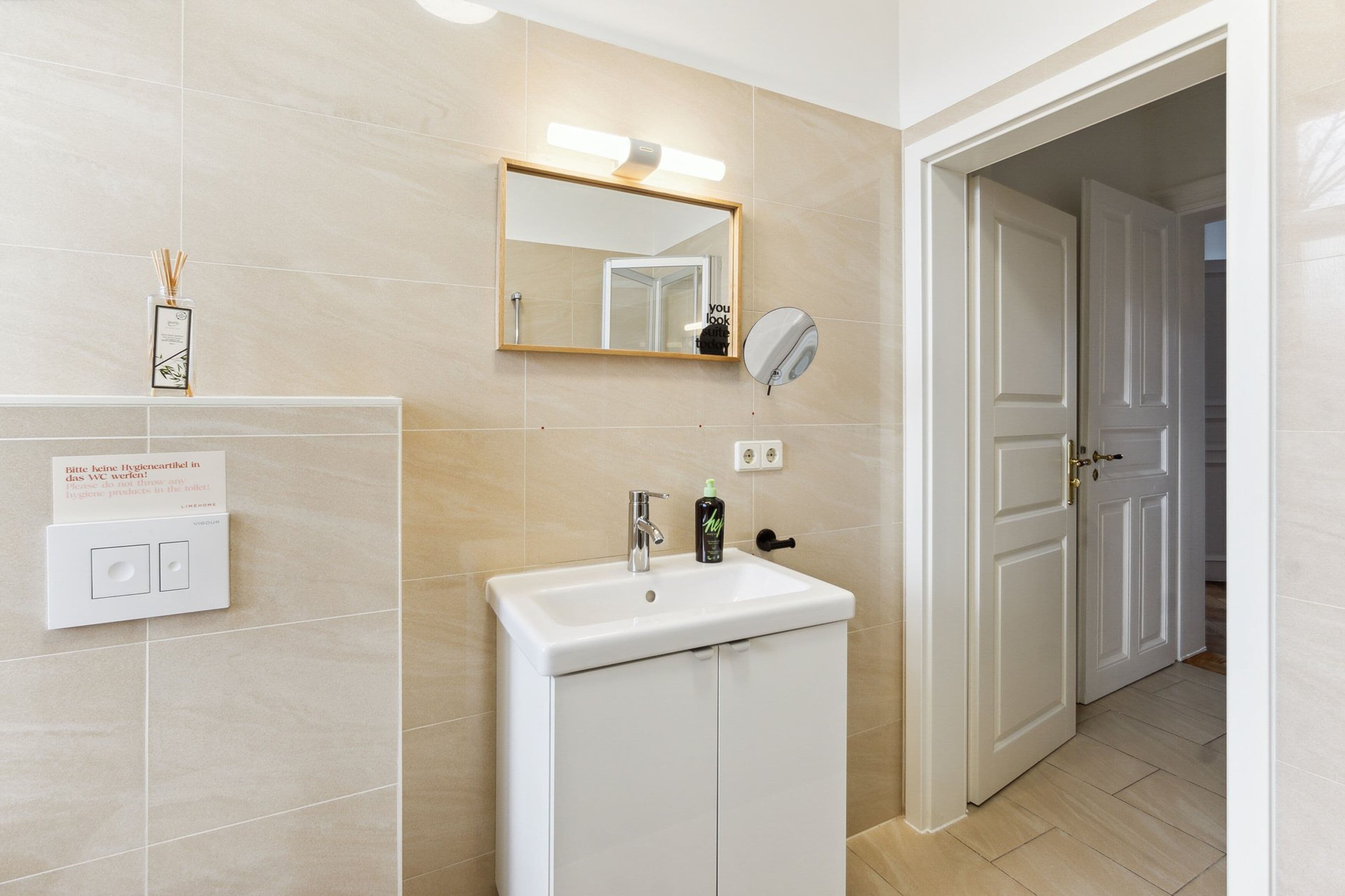 A bathroom with a white sink, a mirror, and a light fixture above it. There is a door leading to another room.