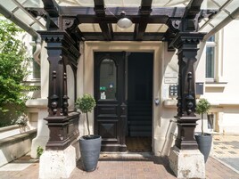 A building entrance with a dark wooden door, a small potted plant, and a metal gate.