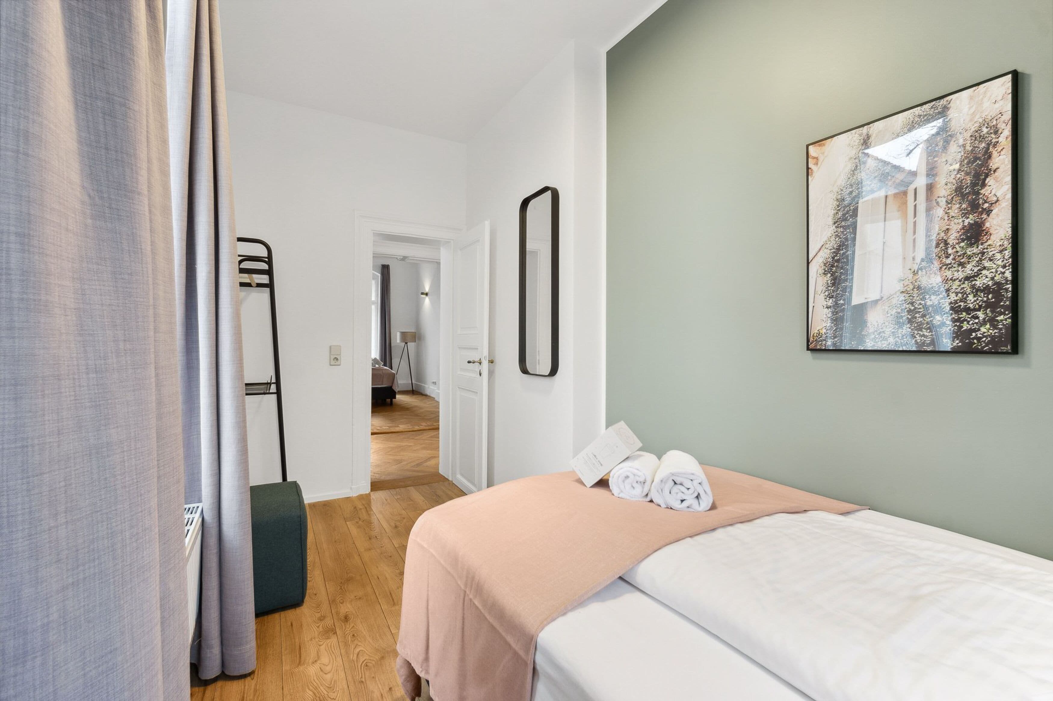 A hotel room with a bed, a painting on the wall, a door leading to another room, and a window with curtains.
