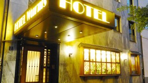 A hotel entrance with a prominent illuminated sign, a set of stairs leading up to the door, and a window with a view of greenery outside. - Hotel Wurms (Düsseldorf)
