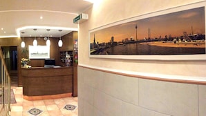 A hotel reception area with a reception desk, a large framed cityscape photograph on the wall, and a staircase leading to another floor. - Hotel Wurms (Düsseldorf)