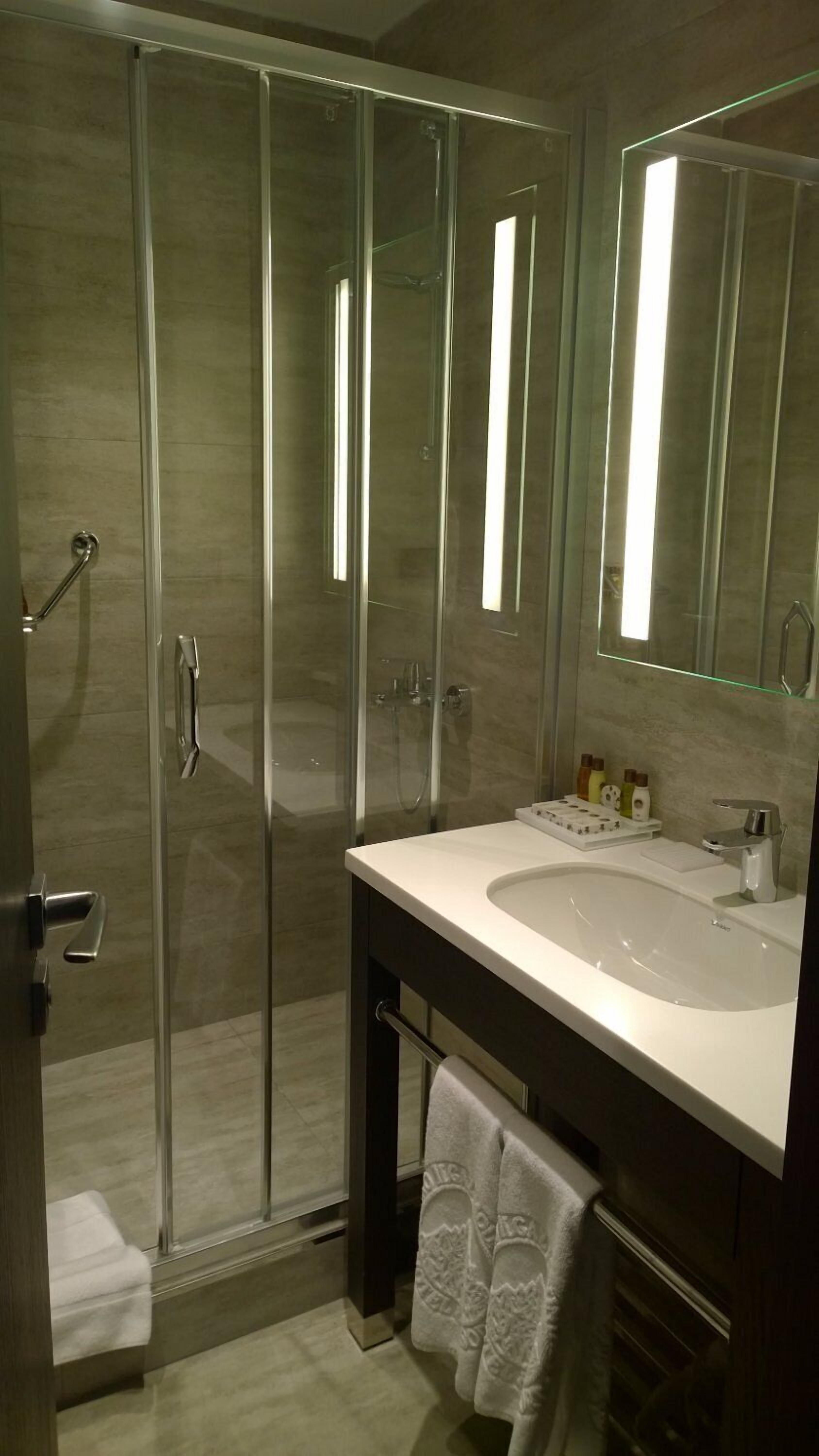 Un baño moderno con ducha envuelta en vidrio, un lavamanos blanco y un espejo grande.