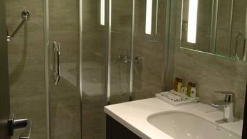 Un baño moderno con ducha envuelta en vidrio, un lavamanos blanco y un espejo grande.