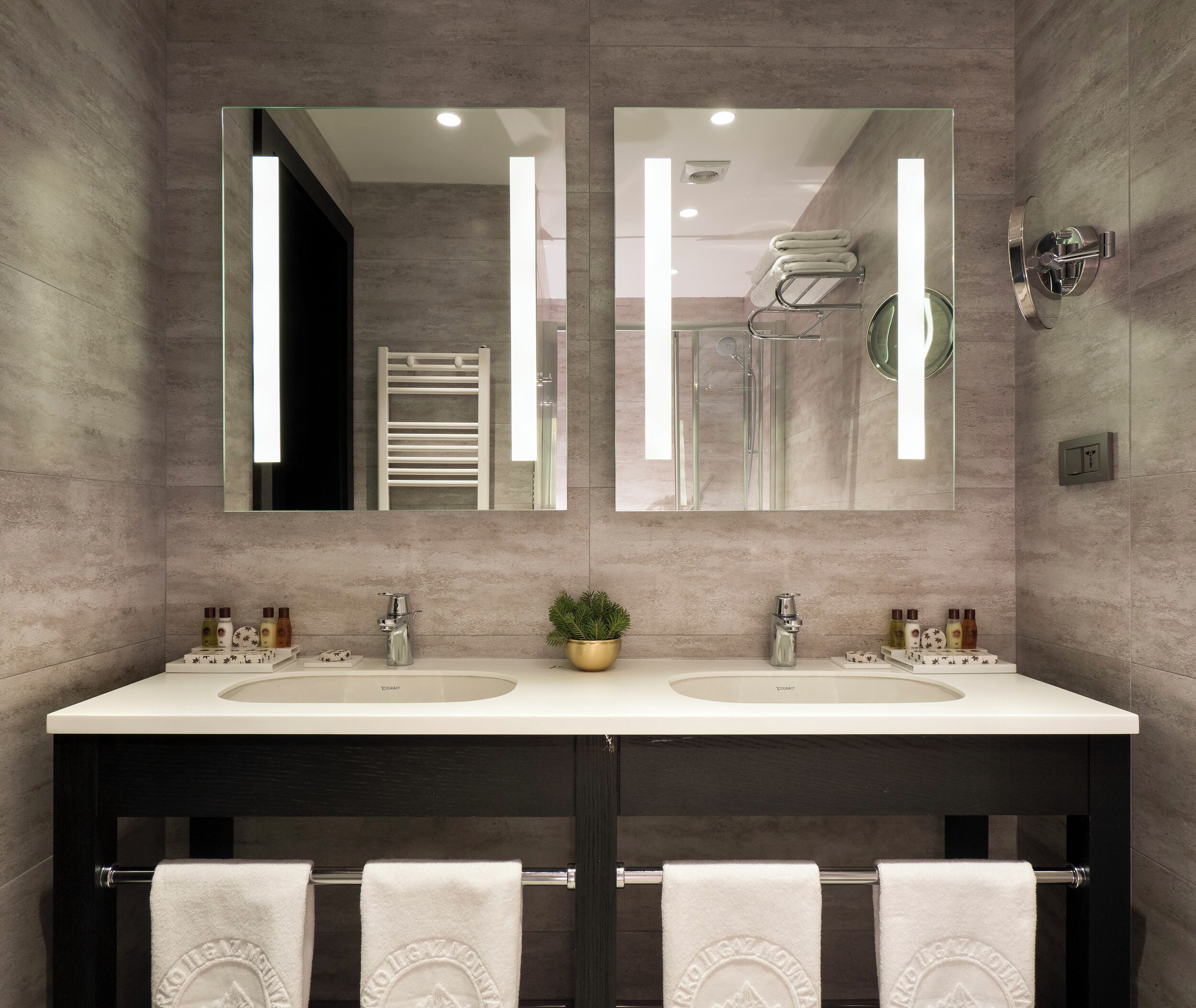 A modern bathroom with two sinks, a large mirror, and a towel rack.