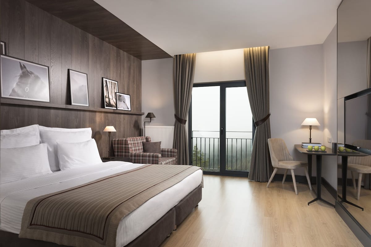 Une chambre d’hôtel avec un grand lit, un bureau avec une chaise, un canapé et un balcon avec des rideaux.