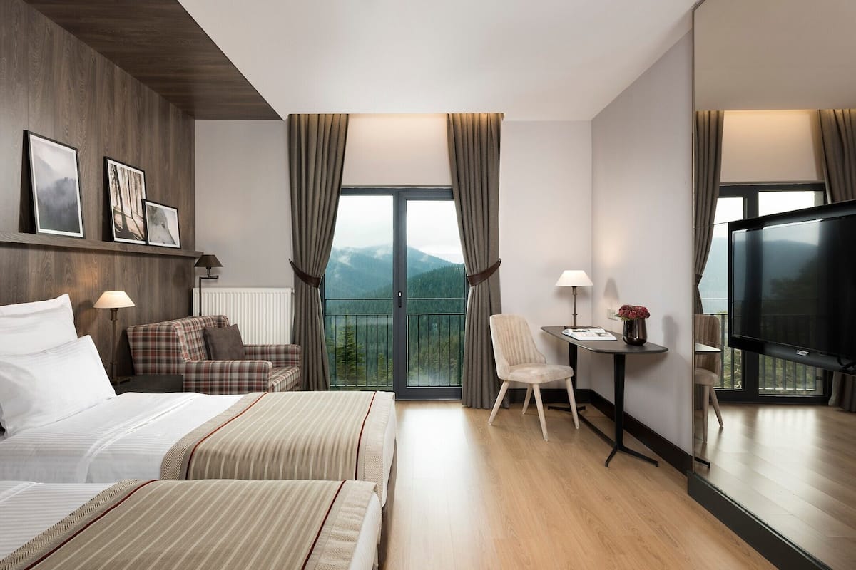 Une chambre d’hôtel comprenant un lit, un canapé, un bureau avec une télévision et un balcon avec des rideaux.