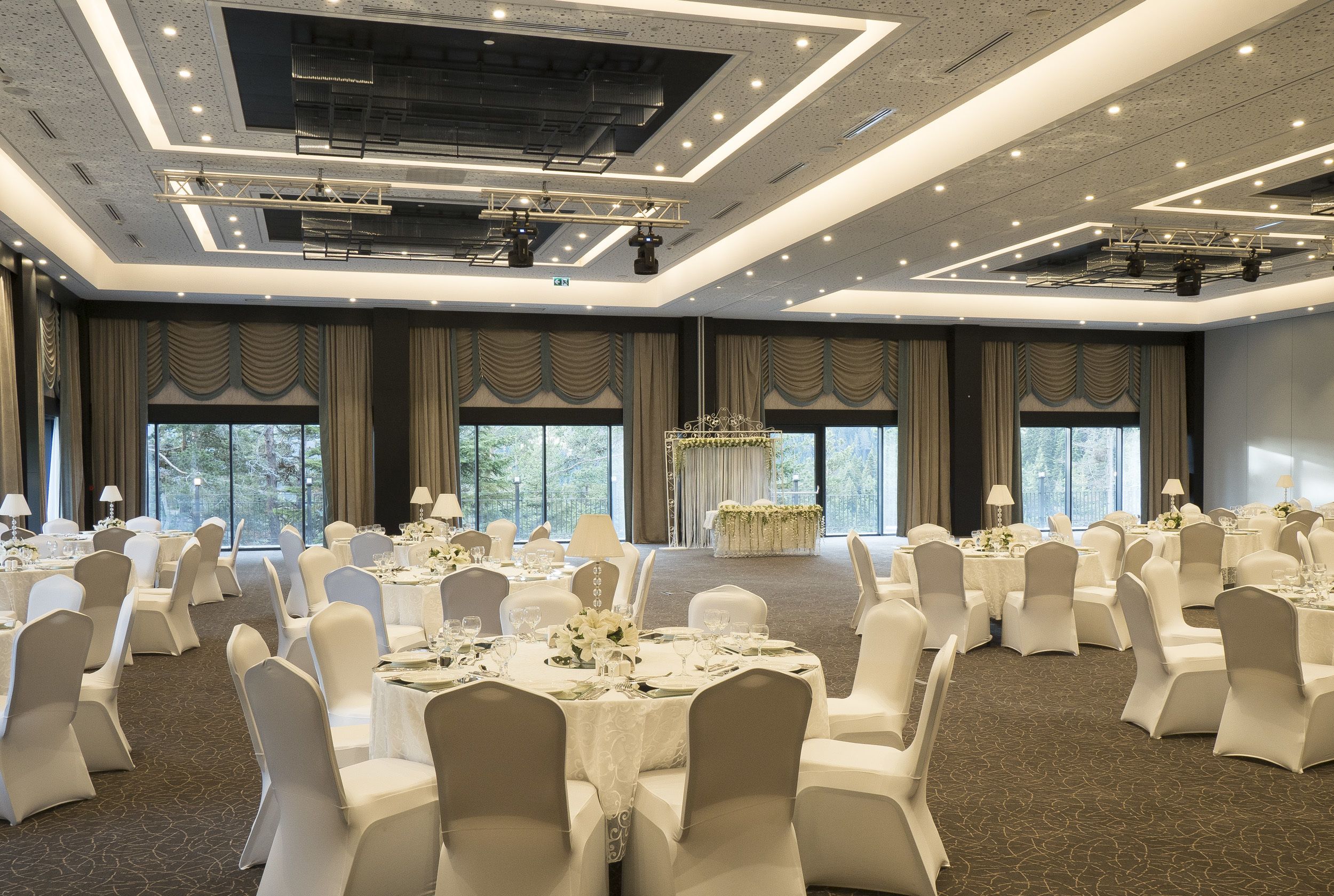 A banquet hall with round tables, white chairs, and a stage with a podium.