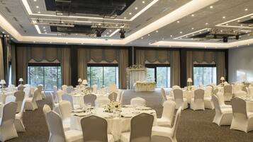 A banquet hall with round tables, white chairs, and a stage with a podium.