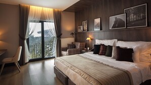 Une chambre d’hôtel avec un grand lit, un bureau, une chaise et une vue sur un paysage enneigé, visible à travers une grande fenêtre.