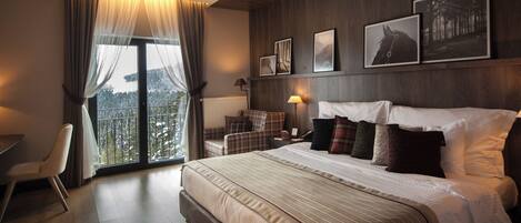 A hotel room with a large bed, a desk, a chair, and a view of a snowy landscape through a large window.