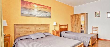 Un dormitorio con dos camas, cabeceros de madera, una mesita de noche, una lámpara, un armario y un cuadro de una puesta de sol sobre el océano.