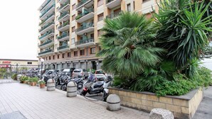 A multi-story residential building with balconies, a parking area with motorcycles, and a variety of potted plants. - Vacanze a Roma (Rome)