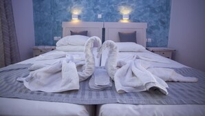 A neatly made bed with white towels arranged in a swan shape, a grey striped blanket, and two wall-mounted lights on a textured blue wall. - Villa Bel Passo (Kos)