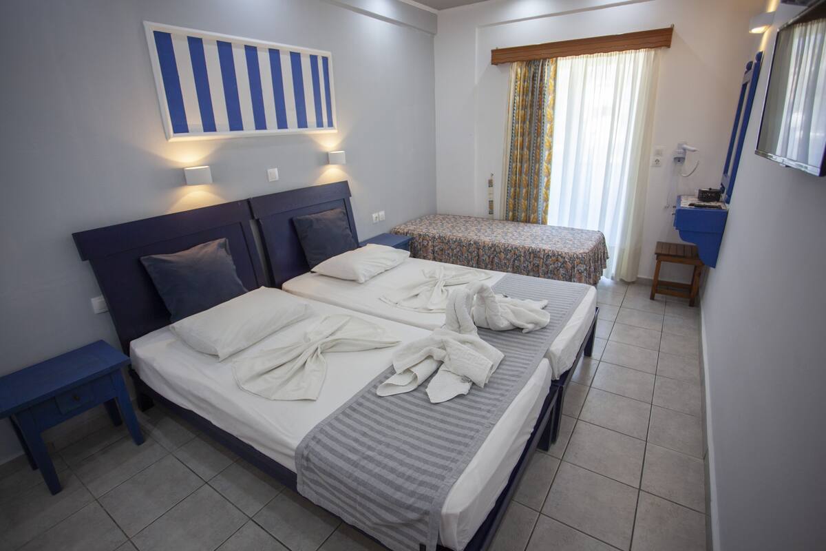 A hotel room with two beds, a small desk, a mirror, and a window with curtains.