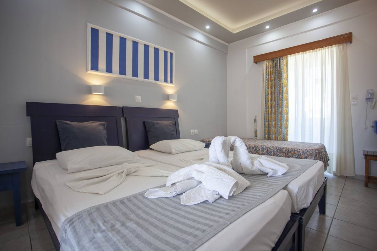 A hotel room with two beds, a large painting on the wall, and a window with curtains.