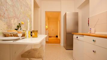A narrow kitchen with a white countertop, a stainless steel refrigerator, and a map on the wall.