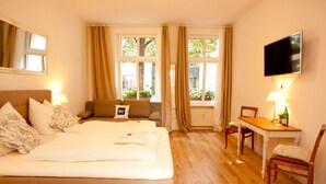 A hotel room with a bed, a desk, a chair, a TV, and large windows with curtains. - Lovely Flats Englische Straße (Berlin)