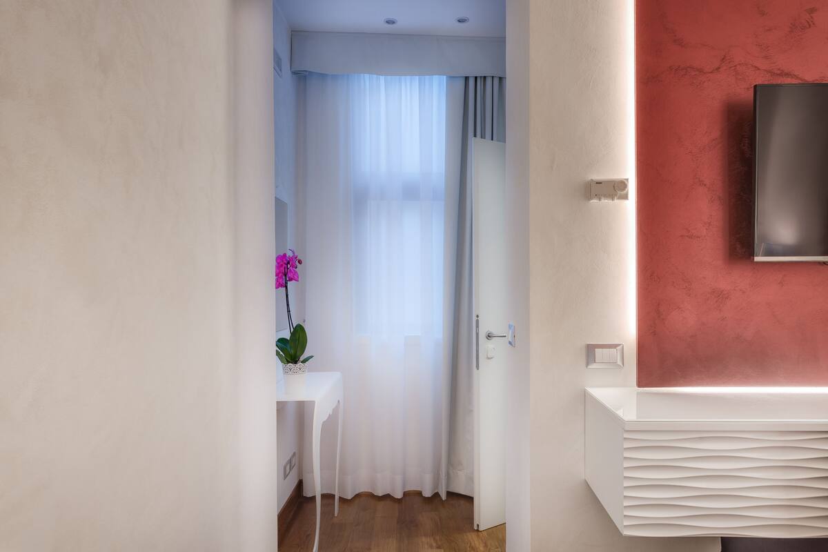 A modern bathroom with a white vanity, a pink orchid, and a red accent wall.