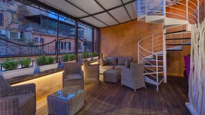 A covered outdoor area with wicker furniture, a spiral staircase, and potted plants. - Shali Luxury Suite (Rome)