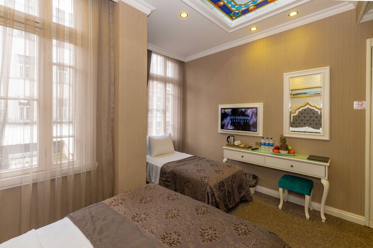 A hotel room with two beds, a desk with a television, and a small bench.